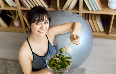Woman eating salad celebrates healthy fitness nutrition. At home after training, she enjoys leafy...