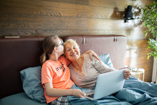 Granddaughter kissing grandmother while using laptop in bed at home
