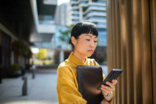 Professional woman checking smartphone outside modern office building