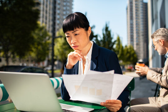 Businesswoman analyzing financial report on laptop at outdoor city cafe