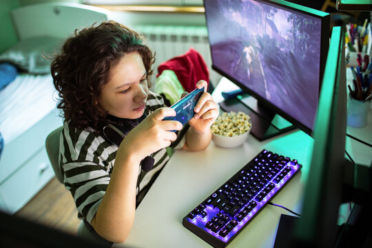 Teen gamer playing mobile game at home desk