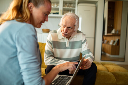 Woman helping elderly man with laptop at home