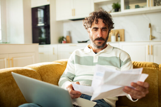 Man reviewing bills with laptop on sofa at home