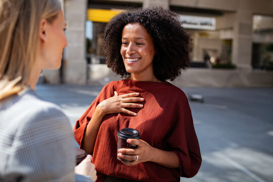 Two women chatting over coffee on city street