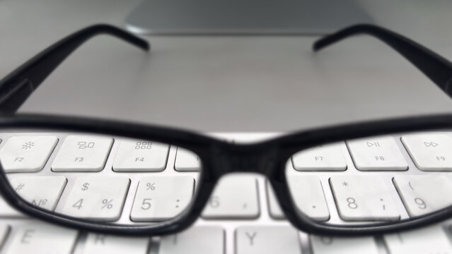 Black eyeglasses resting on a white computer keyboard, workspace detail, office productivity, digital focus, professional tools.