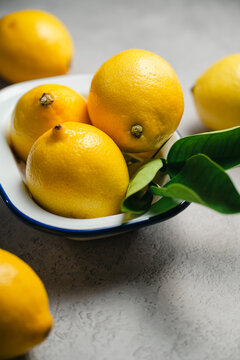 Fresh lemons with green leaves in rustic ceramic bowl on textured gray background, natural citrus fruit still life