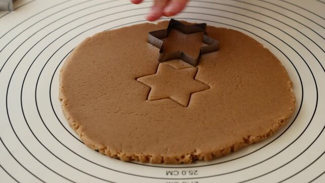 Woman cutting star shaped gingerbread cookie from rolled dough for Christmas baking.