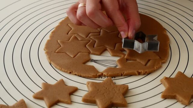Close-up of woman cutting star shaped gingerbread cookies from dough for Christmas baking.