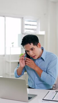 Entrepreneur making a phone call while working on a laptop. Young business man making plans and discussing a new project with a client in an office.