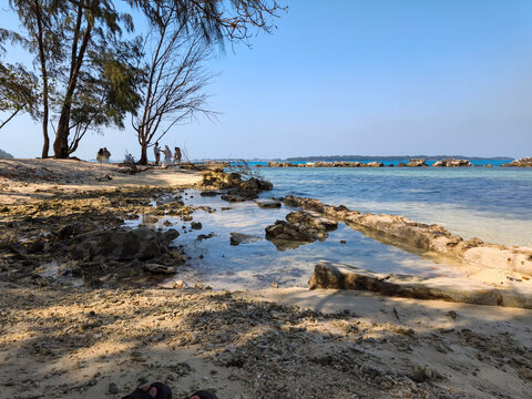 Kepulauan Seribu, Indonesia - 06 September 2026: Tropical beach view with clear sea water, natural coral formations, and tourists under trees.