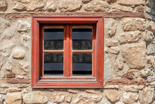A rustic wooden window frame set into an old stone wall of a traditional building.