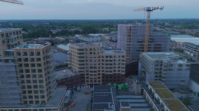 Aerial drone footage flying forward over an urban construction site at dusk, showing apartment buildings under construction, cranes, scaffolding and ongoing city development.