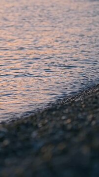 Pebble shore with gentle waves and orange reflections