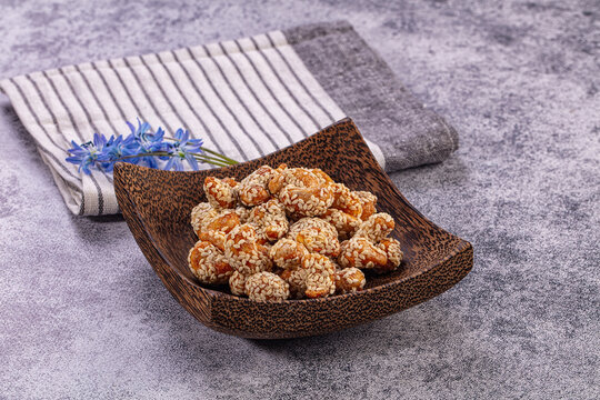 Sesame coated snack pieces in wooden bowl with blue flowers and striped cloth on textured gray surface