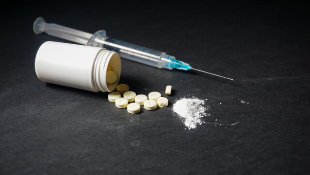One disposable medical syringe in three mililiter size, white powder and several pills spilled from white bottle. Misused drugs concept. 