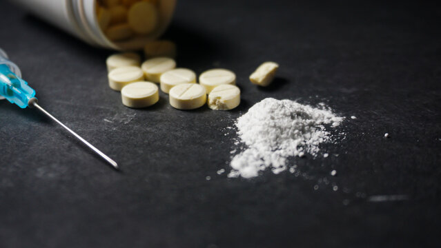 White powder drug, some pills and a syringe on black background. Misused drugs concept. 