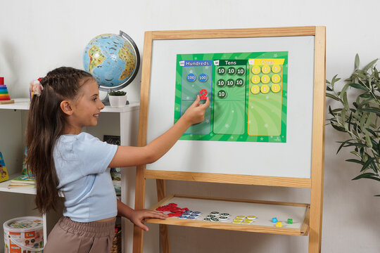 Young schoolgirl practices counting and place value using colorful number tokens for hundreds, tens and ones on a magnetic board in a classroom learning activity.
