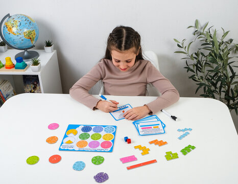 High-quality product shot of a smiling young girl learning fractions at desk. Interactive STEM education layout with colorful math puzzle and word problem cards.