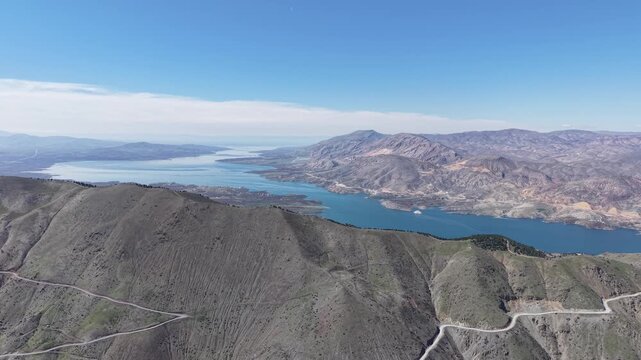 4K static aerial drone shot over a mountain capturing an endless blue river flowing far into the horizon through a majestic valley. Color grading friendly flat profile.