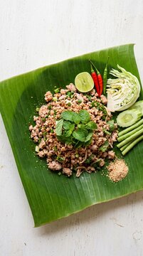 Thai larb minced pork salad flat lay on banana leaf with fresh mint and chilies, vibrant authentic Isaan food concept