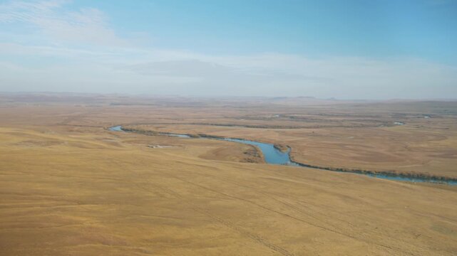 A handheld camera pans right over the winding Bely Iyus river and vast autumn plains in Khakassia, Russia. 