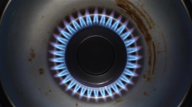 Top View of Gas Stove Burner with Blue Flame Increasing Around Circular Ring