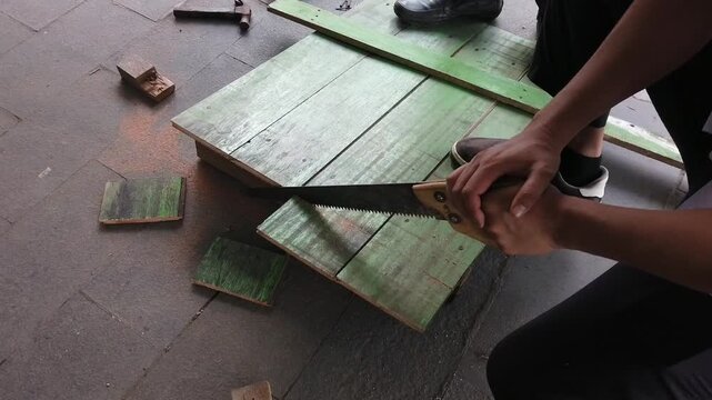 A person sawing a wooden board with a hand saw. The video shows manual woodworking activity related to carpentry, construction, home improvement, repair, and practical craftsmanship.
