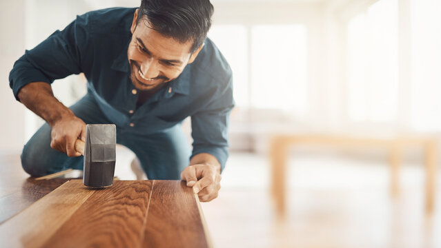 Smiling carpenter installing hardwood oak floor planks with rubber mallet background banner