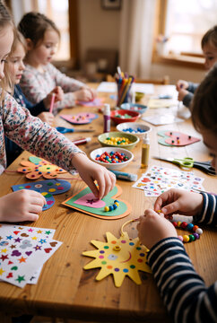 Group of children making arts and crafts at table. Kids decorating paper shapes with beads and stickers. Learning and DIY activity concept