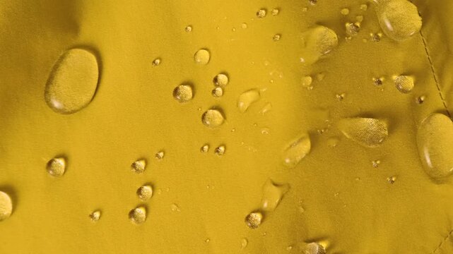 Water drops are dripping on yellow hydrophobic fabric.