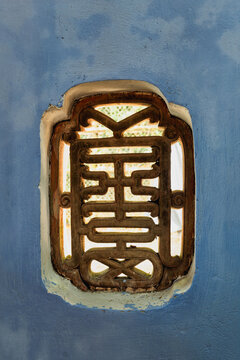 Ornate wooden window lattice at Hon Chen Shrine in Hue, Vietnam. A detail shot of traditional architectural carvings set within a blue-painted wall of the historic site