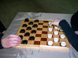 Male and female hands moving black and white round checkers pieces during strategic logic game tournament on classic wooden checkered board © Dmitry