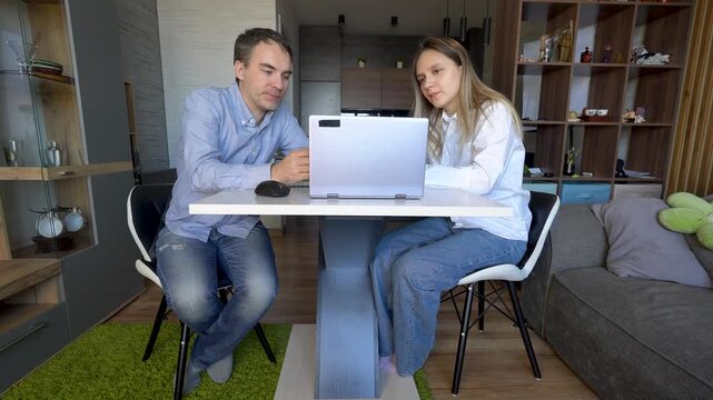 Tutor teaching student pointing at laptop screen. Two colleagues working on task together using computer and internet.