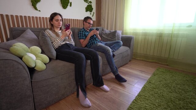 Couple sitting on a sofa, both looking at their smartphones, physically together but emotionally distant. Digital loneliness, screen addiction, and lack of real communication.