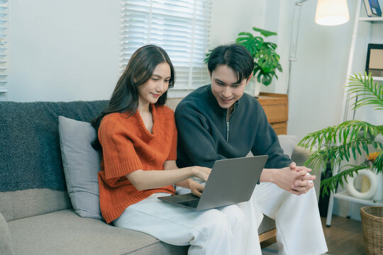 Happy Asian couple using laptop and smartphone together at home