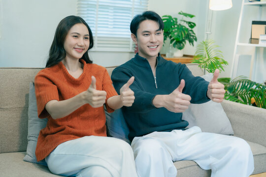 Happy Asian couple sitting on sofa talking and gesturing together at home