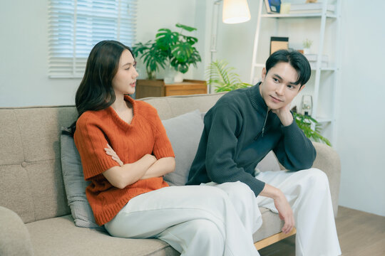 Happy Asian couple sitting on sofa talking and gesturing together at home