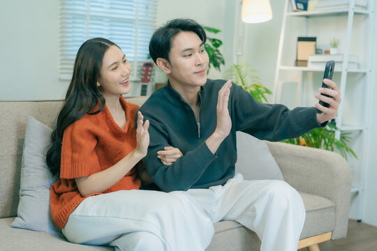 Happy Asian couple sitting on sofa talking and gesturing together at home