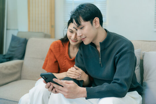 Happy Asian couple sitting on sofa talking and gesturing together at home