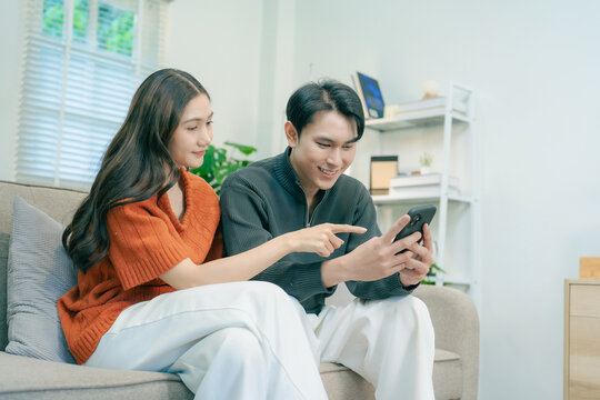 Happy Asian couple sitting on sofa talking and gesturing together at home