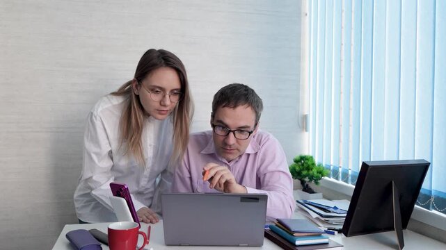 Businessman and businesswoman analyzing data on a laptop, discussing strategy and work processes. Professional collaboration, strategic planning, and teamwork in a modern office.