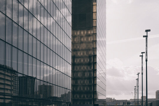 Modern urban architecture uses a glass facade and reflections beside a row of lamps where perspective and lines define the exterior