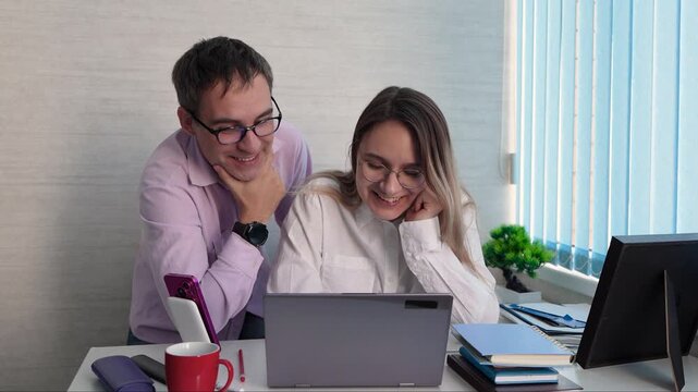 Joyful colleagues celebrating a business success while looking at a laptop screen. The man laughs in disbelief and the woman cheers in excitement. Shared victory, motivated team, and positive corporat