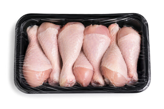 Six pieces of raw chicken drumsticks are arranged in a plastic tray. The tray is wrapped in clear plastic. The setting is a grocery store where fresh meat is sold.
