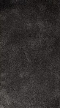 Muted monochrome texture in real filming. Dark textured drifts slowly in moody abstract style, forming soft swirling patterns across black space.