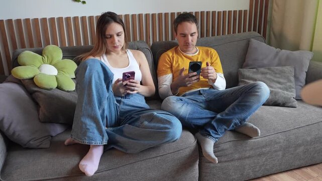 Couple sitting on a sofa, both looking at their smartphones, physically together but emotionally distant. Digital loneliness, screen addiction, and lack of real communication.