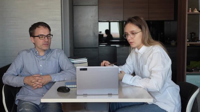 Tutor teaching student pointing at laptop screen. Two colleagues working on task together using computer and internet.