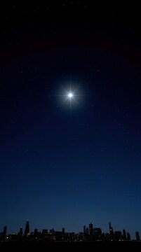 Bright star shining high in the deep blue night sky above a distant city skyline.