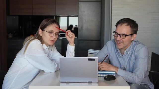 Young couple working at home on a laptop, solving a difficult task together, deep in thought and focused on problem.