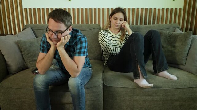 Young married couple sitting on a sofa with crossed arms, refusing to talk to each other. Family conflict, resentment, and silent treatment.